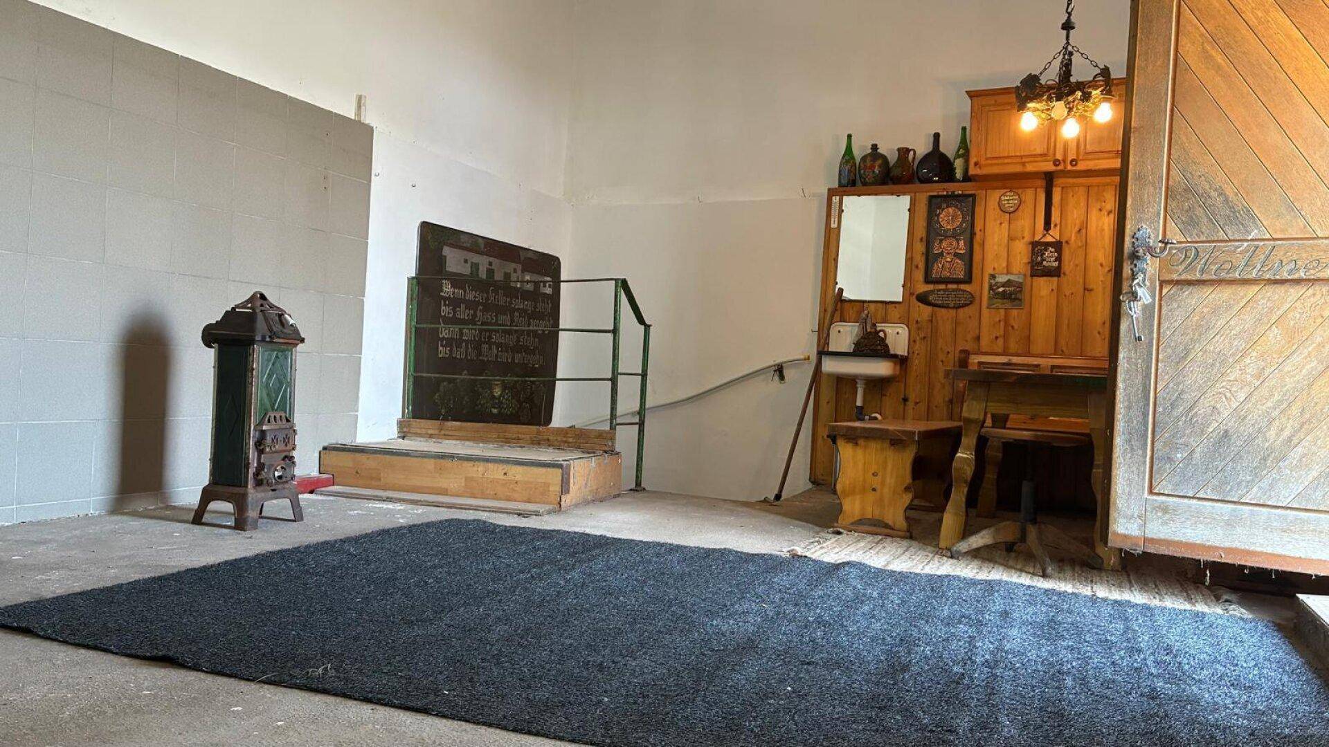Rustikaler Innenraum mit Holzeinbauten, einem Ofen und einem Teppich auf Betonboden.