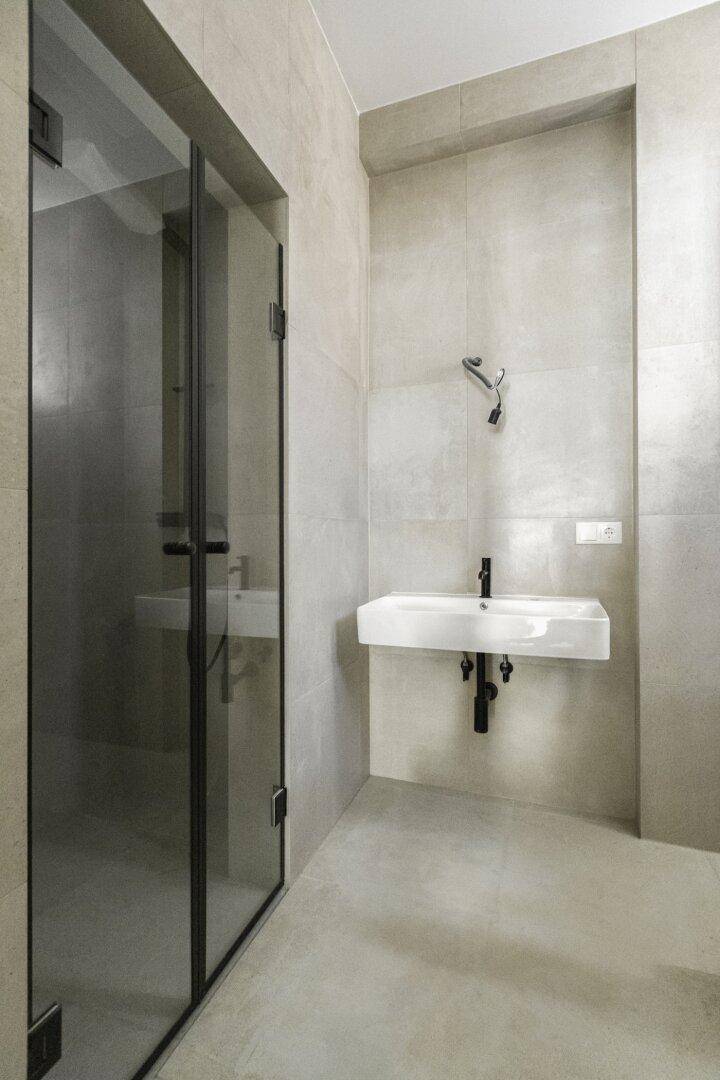 Modernes Badezimmer mit grauen Fliesen, wandhängendem Waschbecken und einer begehbaren Glasdusche.