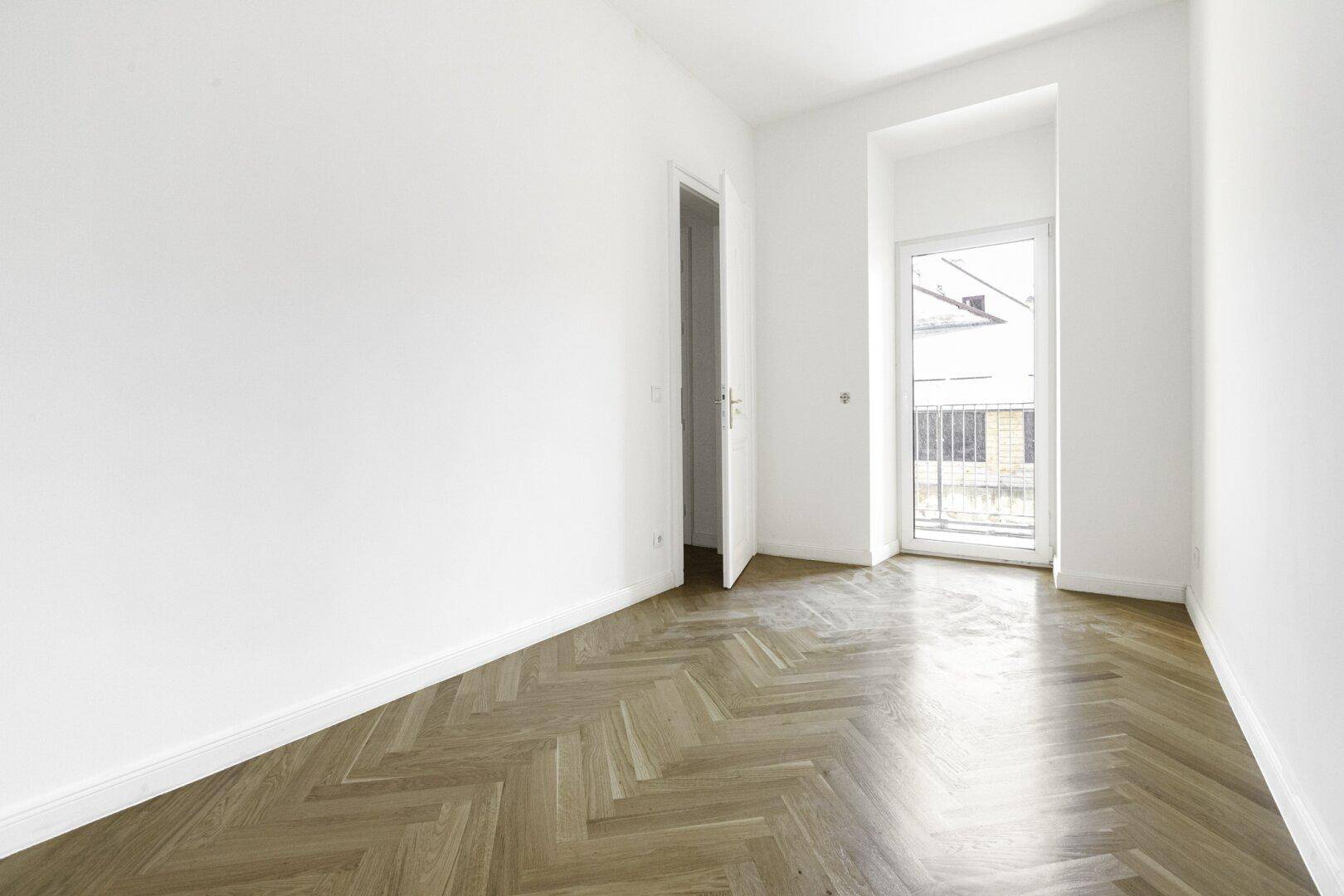 Helles Zimmer mit Fischgrätparkett und Zugang zu einem französischen Balkon.
