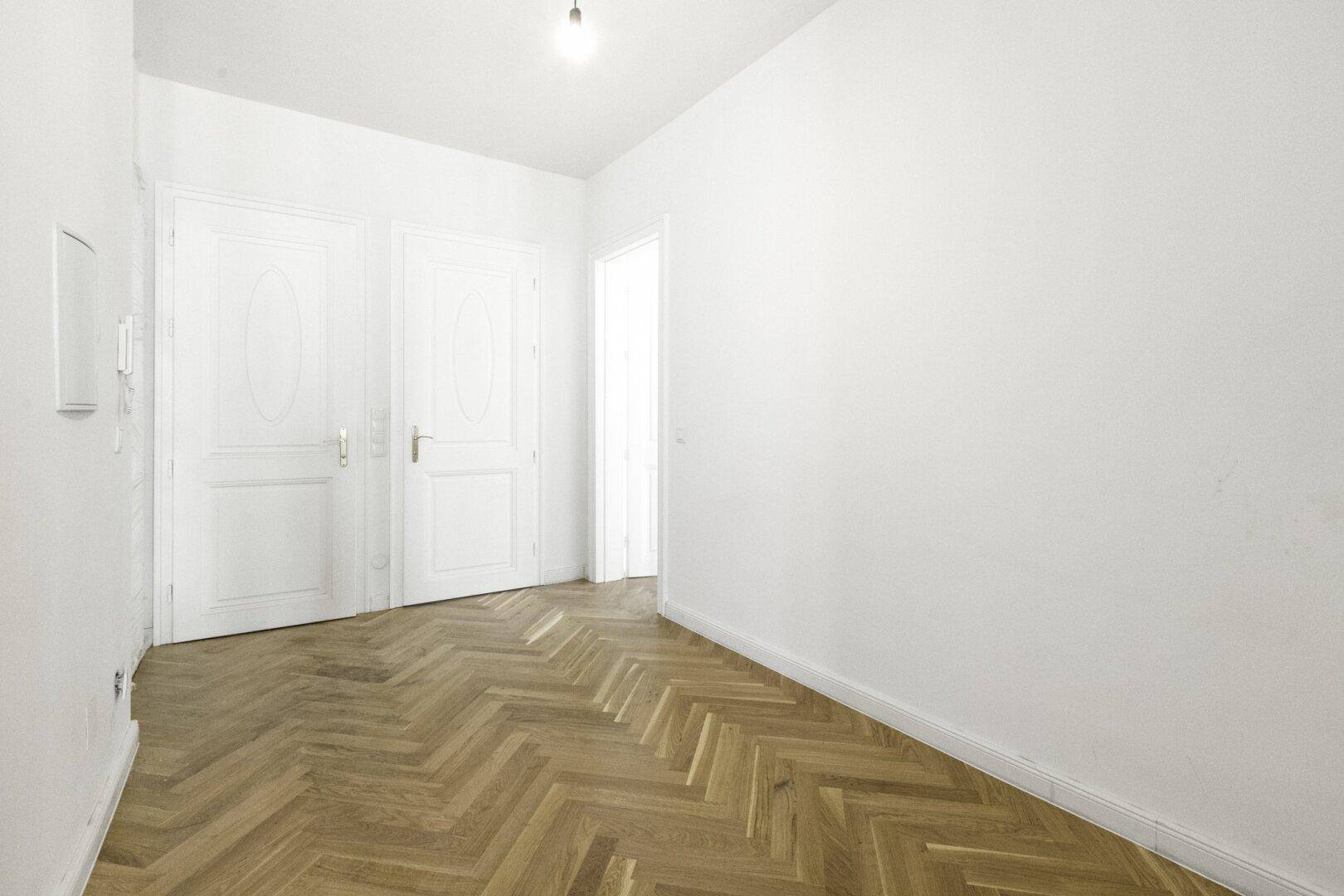 Eingangsbereich mit Fischgrätparkett und zwei eleganten weißen Flügeltüren.