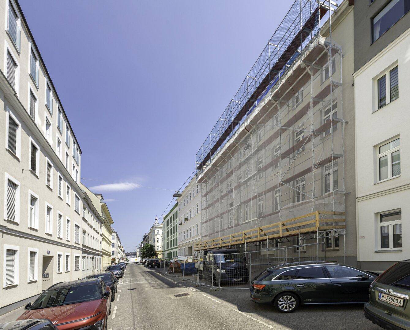 Straßenansicht mit einem Gebäude, das sich im Umbau befindet und eingerüstet ist.