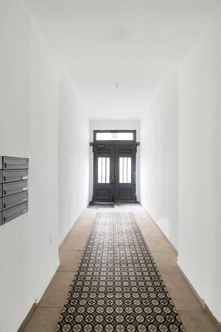 Eingangsbereich mit gemustertem Teppichläufer und dunkler Holztür am Ende des Flurs.