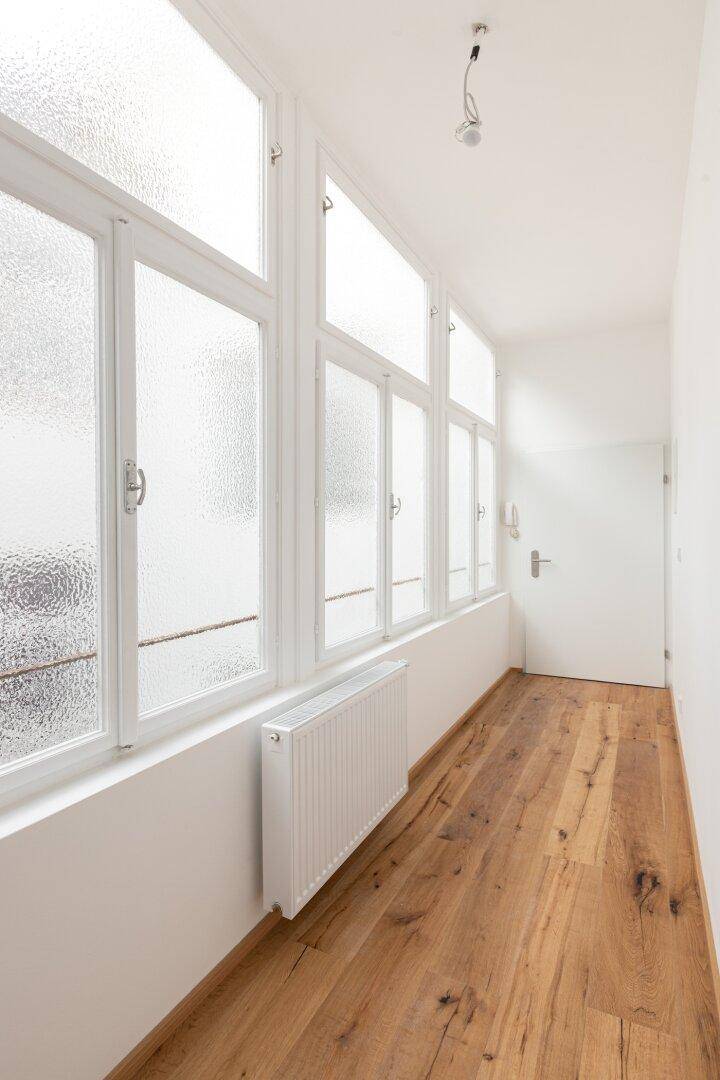Heller Flur mit Holzboden und einer Reihe von Fenstern, die für natürliches Licht sorgen.