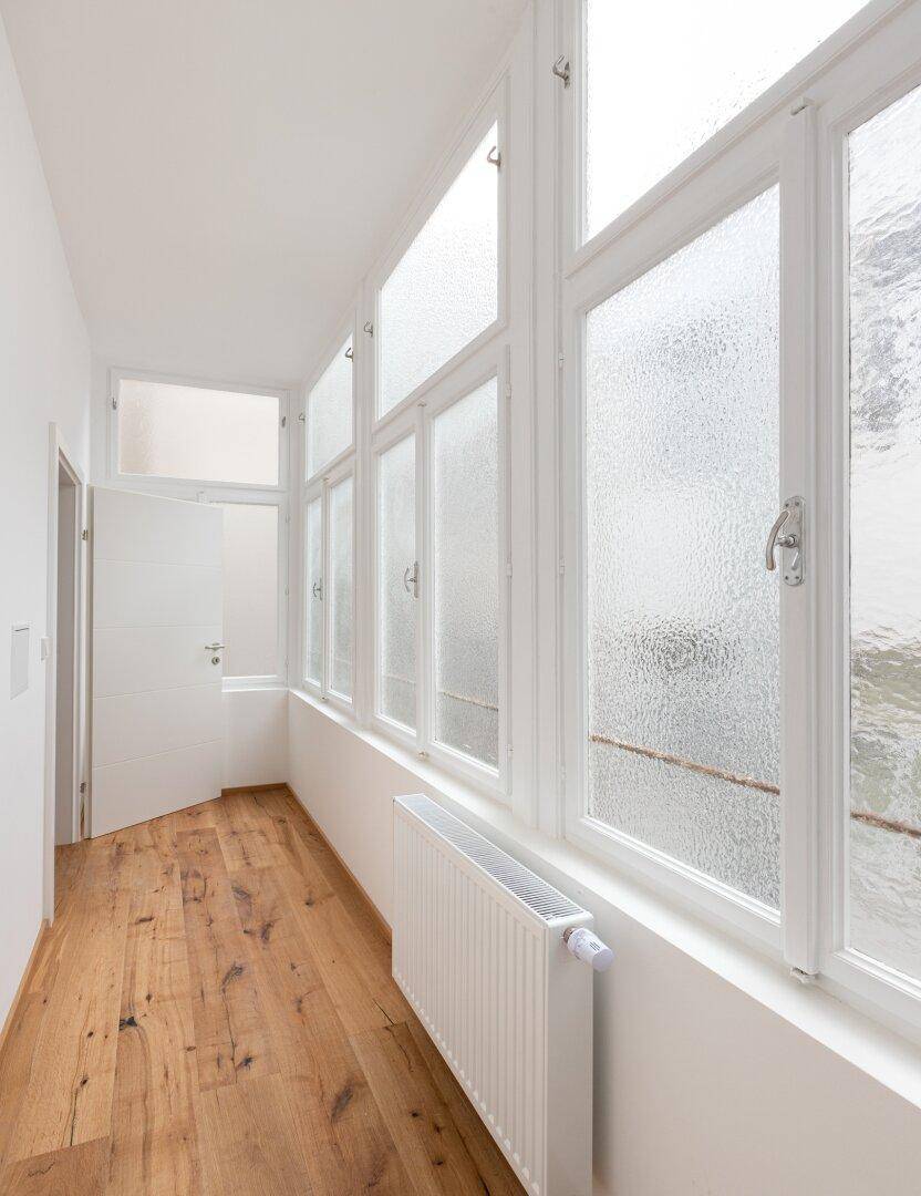 Langer Flur mit Holzboden und mehreren Fenstern, die für eine helle und freundliche Atmosphäre sorgen.