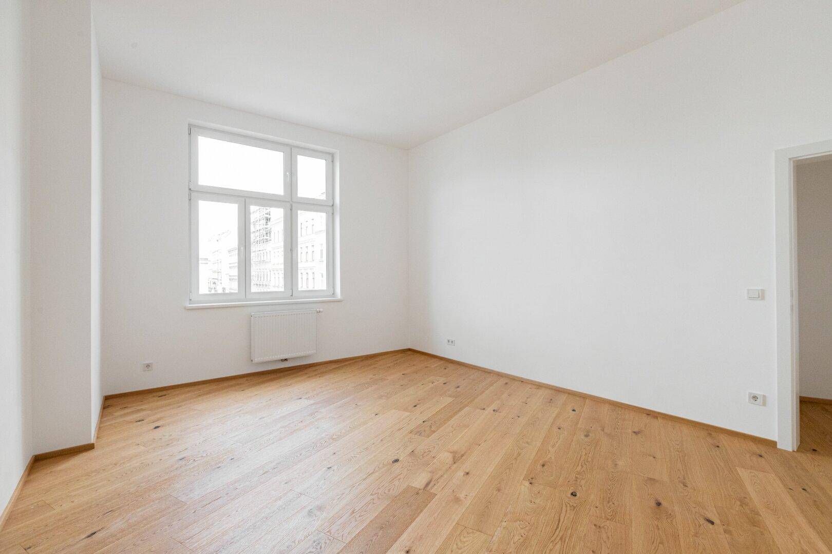 Helles, leeres Zimmer mit Parkettboden und einem großen Fenster, bereit zur individuellen Gestaltung.