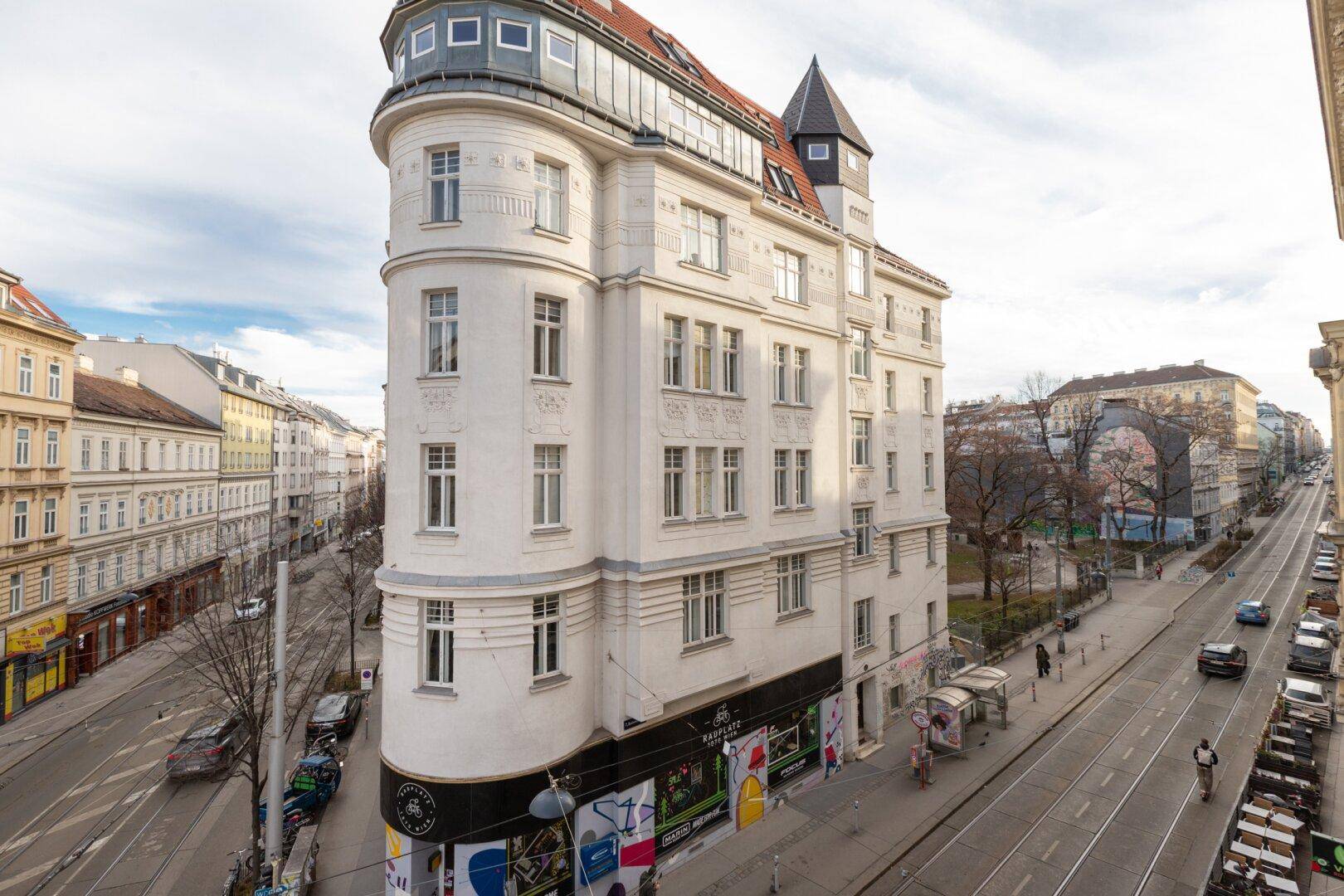 Historisches Eckgebäude mit markanter Architektur und Geschäften im Erdgeschoss an einer belebten Straße.