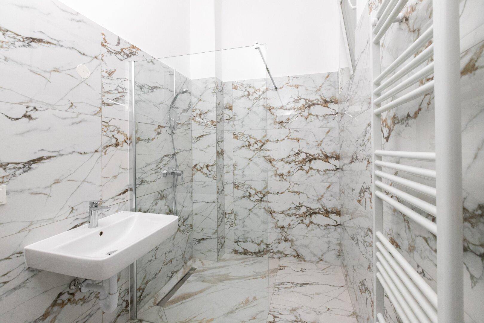 Modernes Badezimmer mit Marmorfliesen, ebenerdiger Dusche und beheiztem Handtuchhalter.
