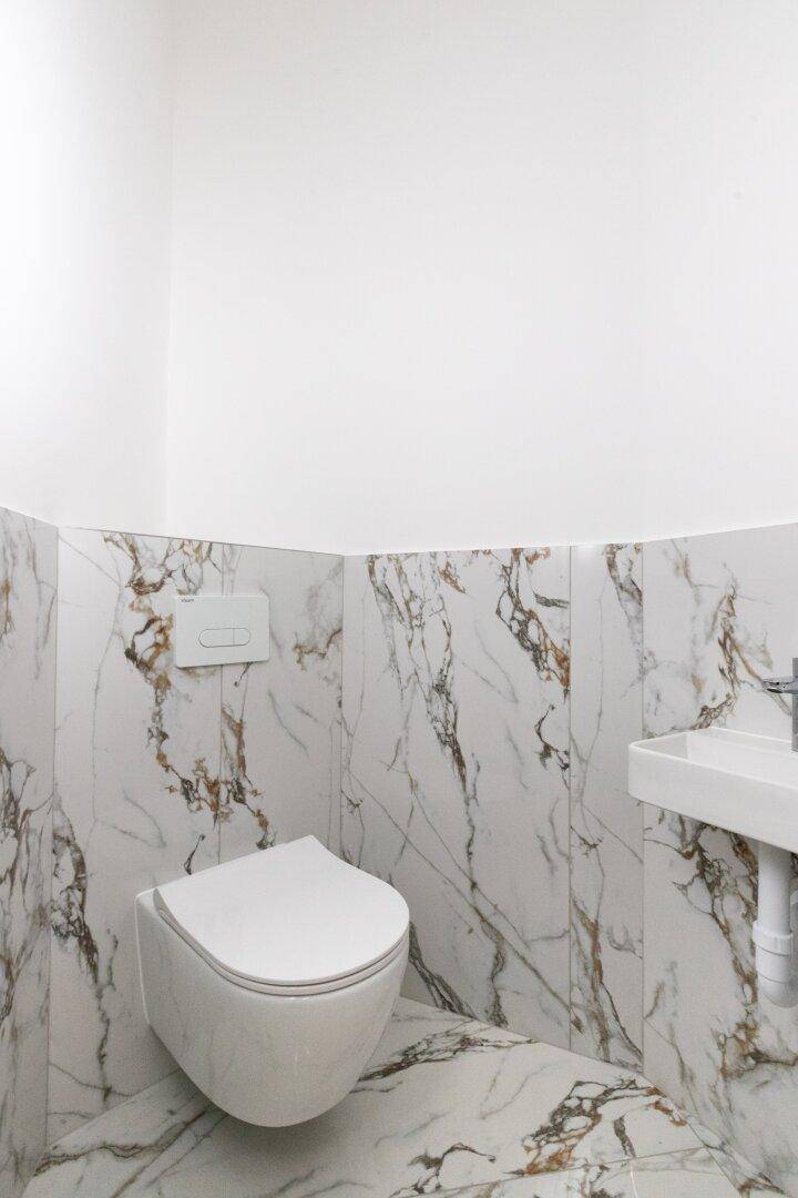 Separate Gästetoilette mit modernen Marmorfliesen, wandhängendem WC und kleinem Waschbecken.