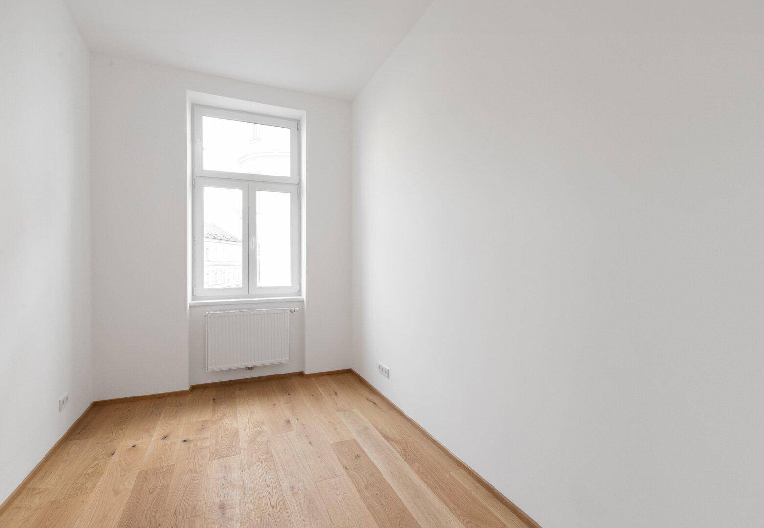 Gemütliches, leeres Zimmer mit Parkettboden und einem Fenster, ideal für ein Schlafzimmer oder Büro.