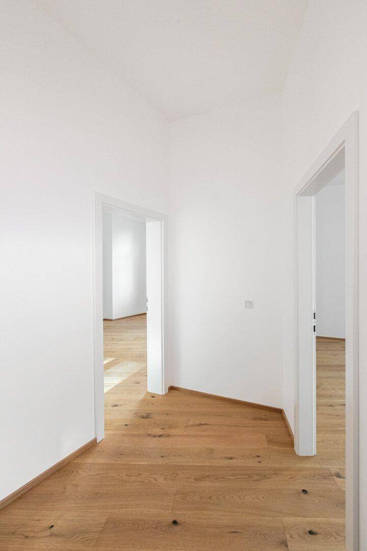 Heller Flur mit Parkettboden und weißen Wänden, der zu verschiedenen Zimmern führt.