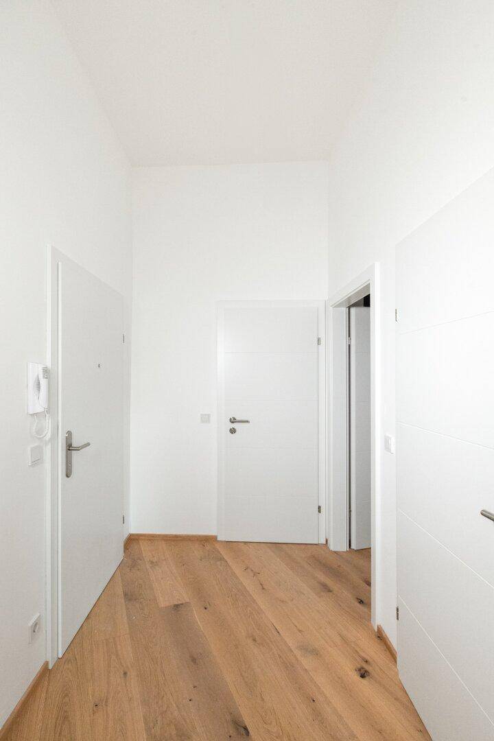 Eingangsbereich mit Parkettboden, weißen Türen und Gegensprechanlage, hell und einladend.