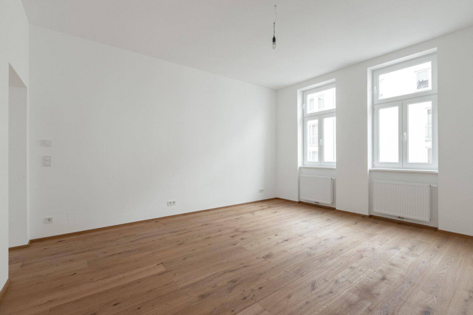 Heller, unmöblierter Raum mit Holzboden und zwei Fenstern, ideal für Wohnzwecke.