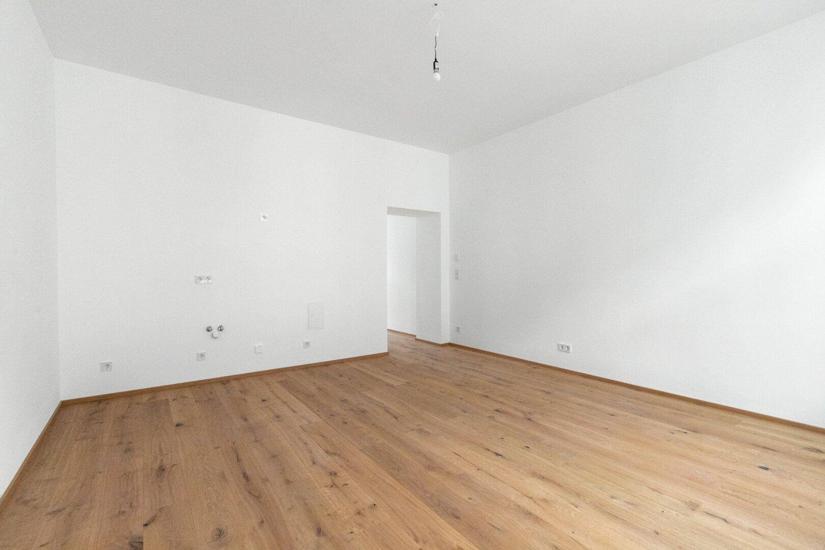 Leerer Raum mit Holzboden und vorbereiteten Anschlüssen an der Wand für zukünftige Nutzung.