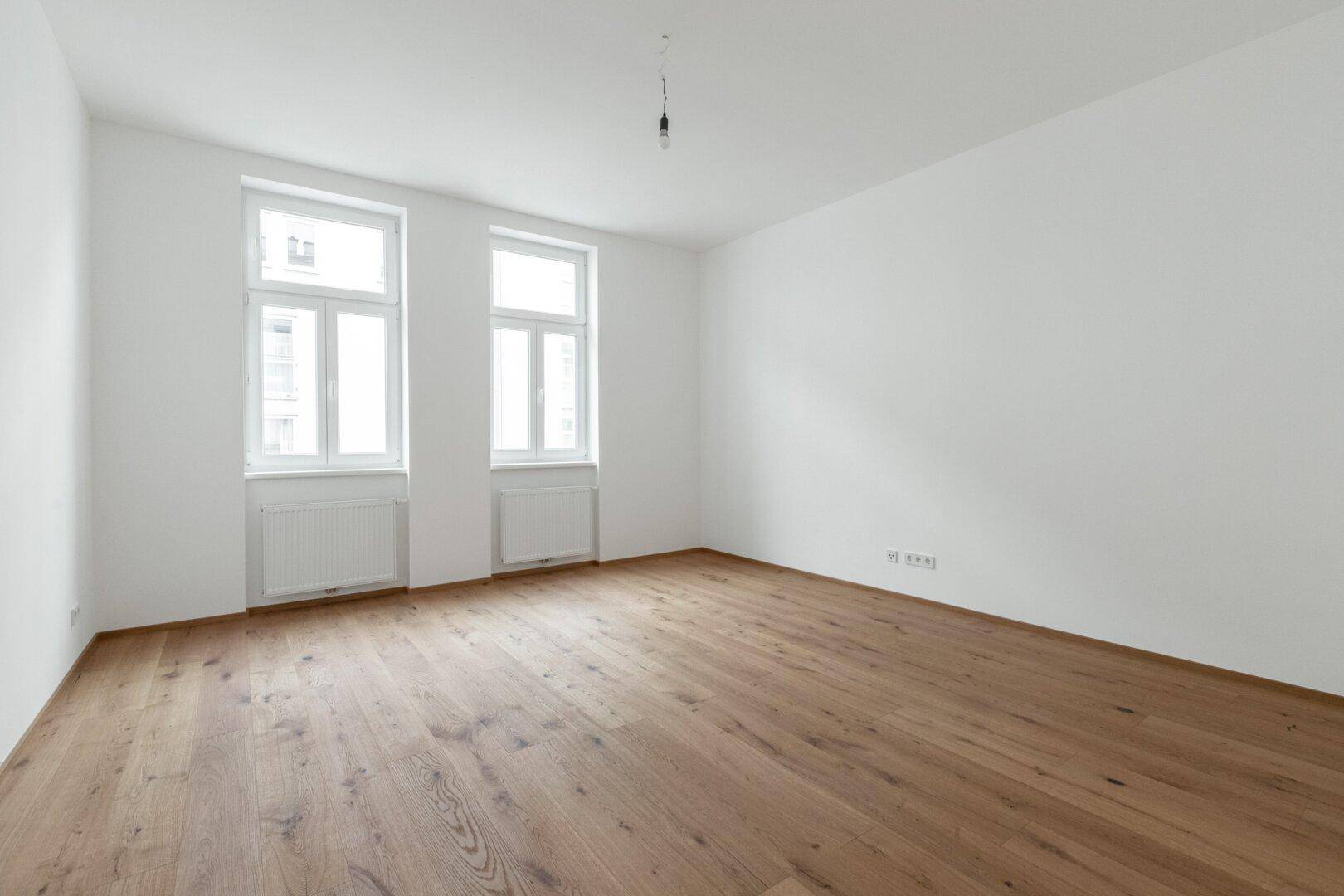 Geräumiger, leerer Raum mit Holzboden und großen Fenstern, bereit zur individuellen Einrichtung.