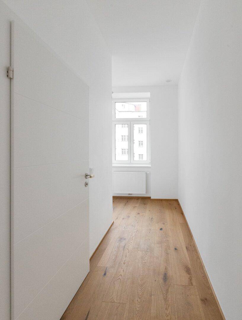 Langer, heller Flur mit Holzboden und einer modernen weißen Tür, die zum nächsten Raum führt.