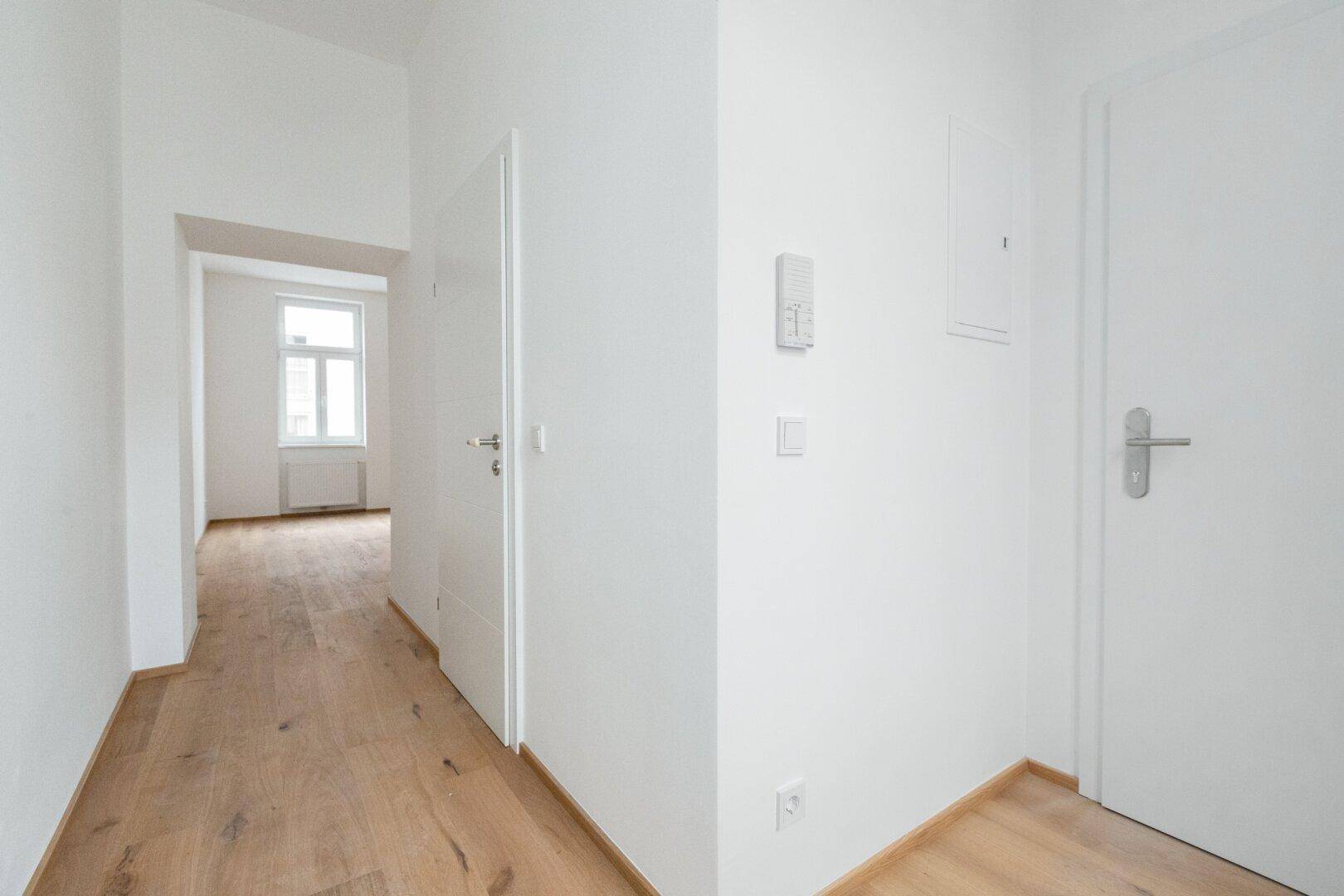 Heller Eingangsbereich mit Holzboden und mehreren weißen Türen, die zu verschiedenen Räumen führen.
