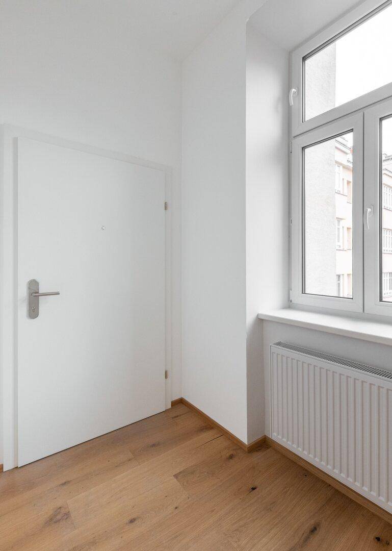 Helle Ecke im Flur mit Fenster und Heizkörper, die viel Tageslicht hereinlässt.