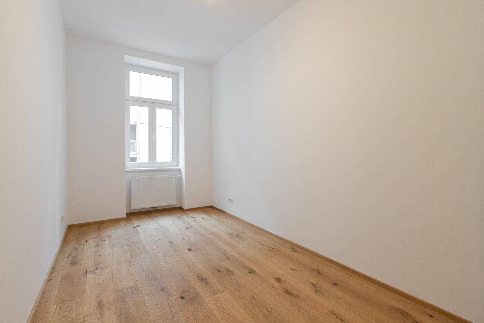 Ruhiges Schlafzimmer mit Holzboden und einem großen Fenster, bietet viel natürliches Licht.