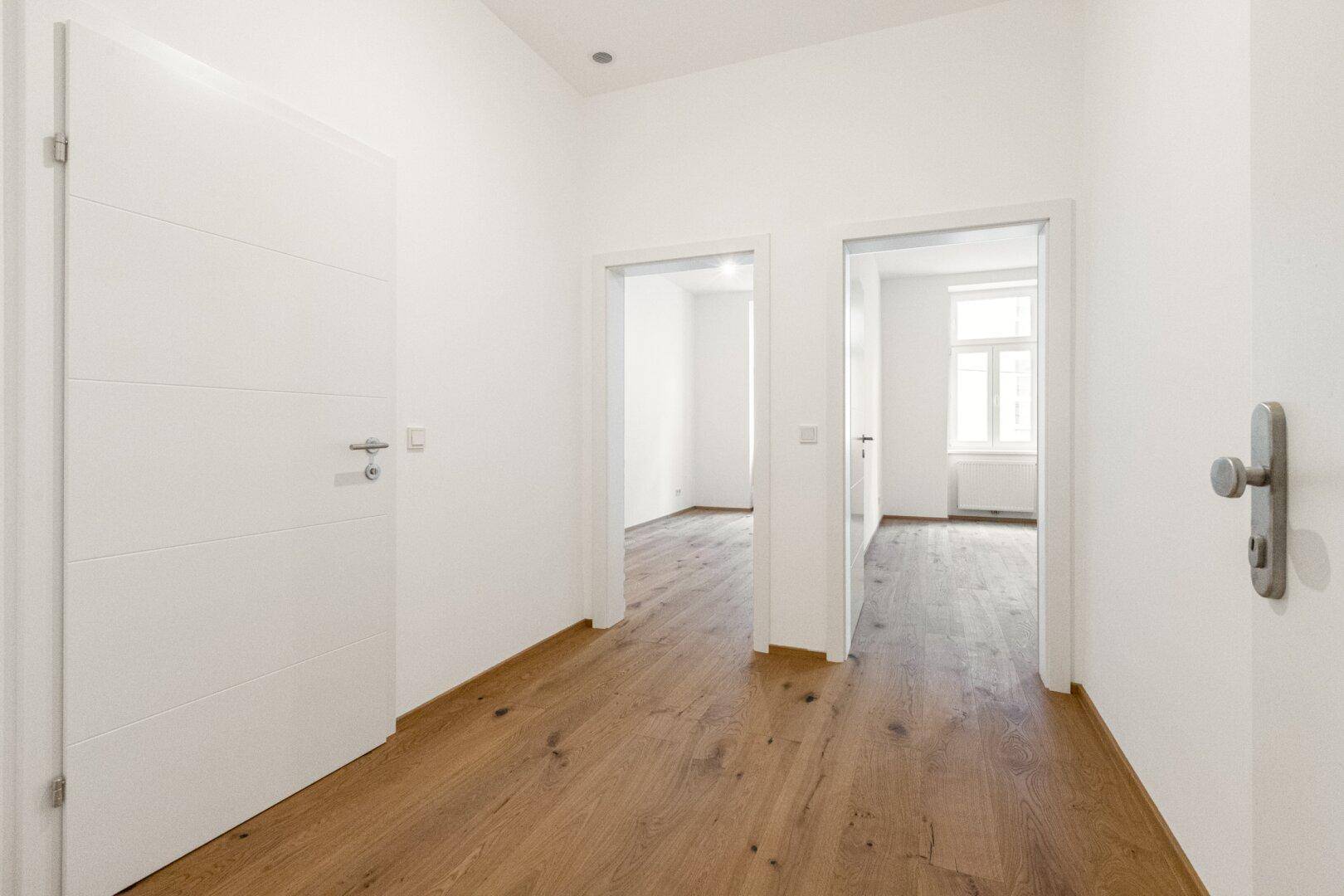 Heller Flur mit Holzboden und weißen Türen, der zu verschiedenen Räumen der Wohnung führt.