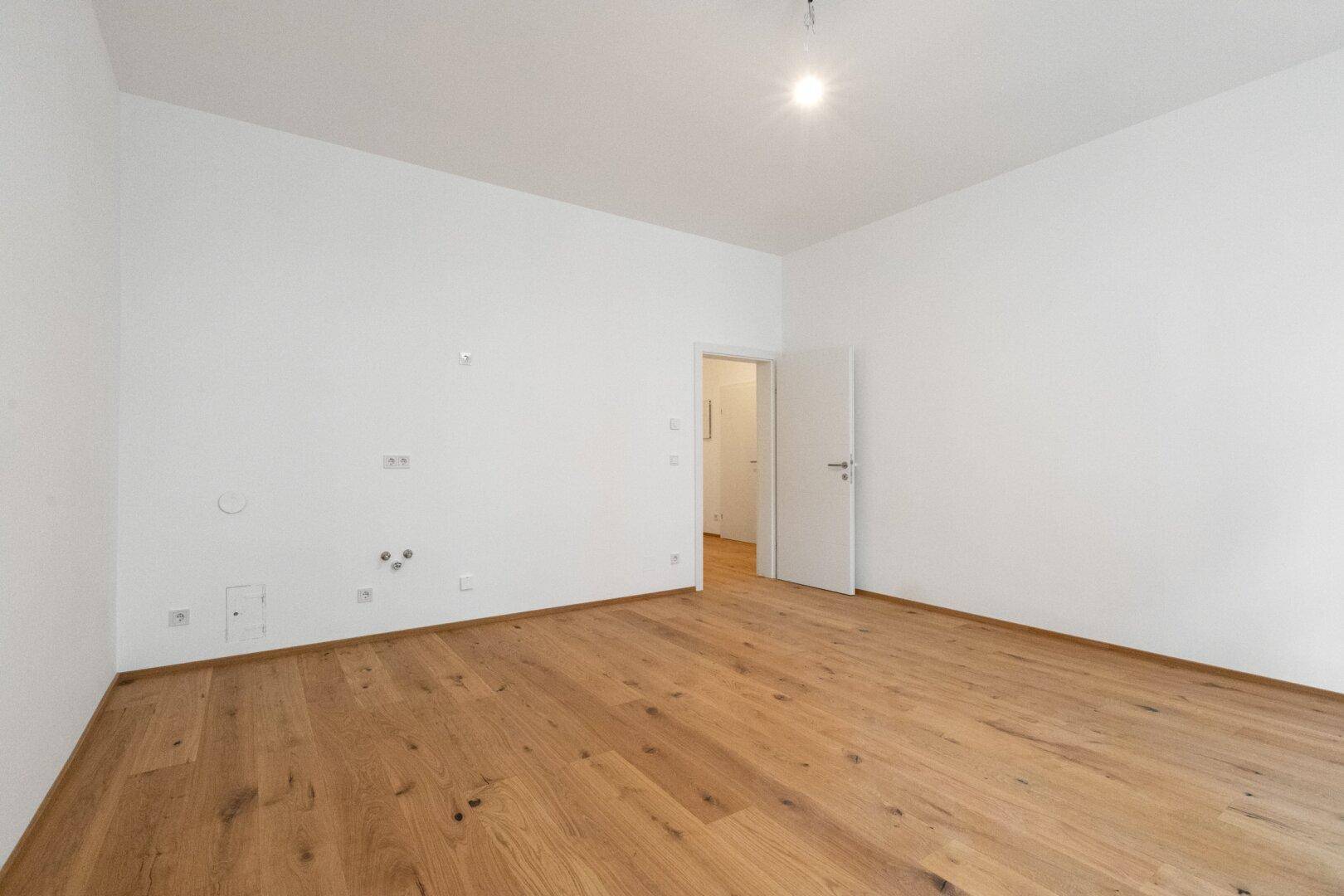 Heller, unmöblierter Raum mit Holzboden und offener Tür, ideal für ein Schlafzimmer oder Büro.