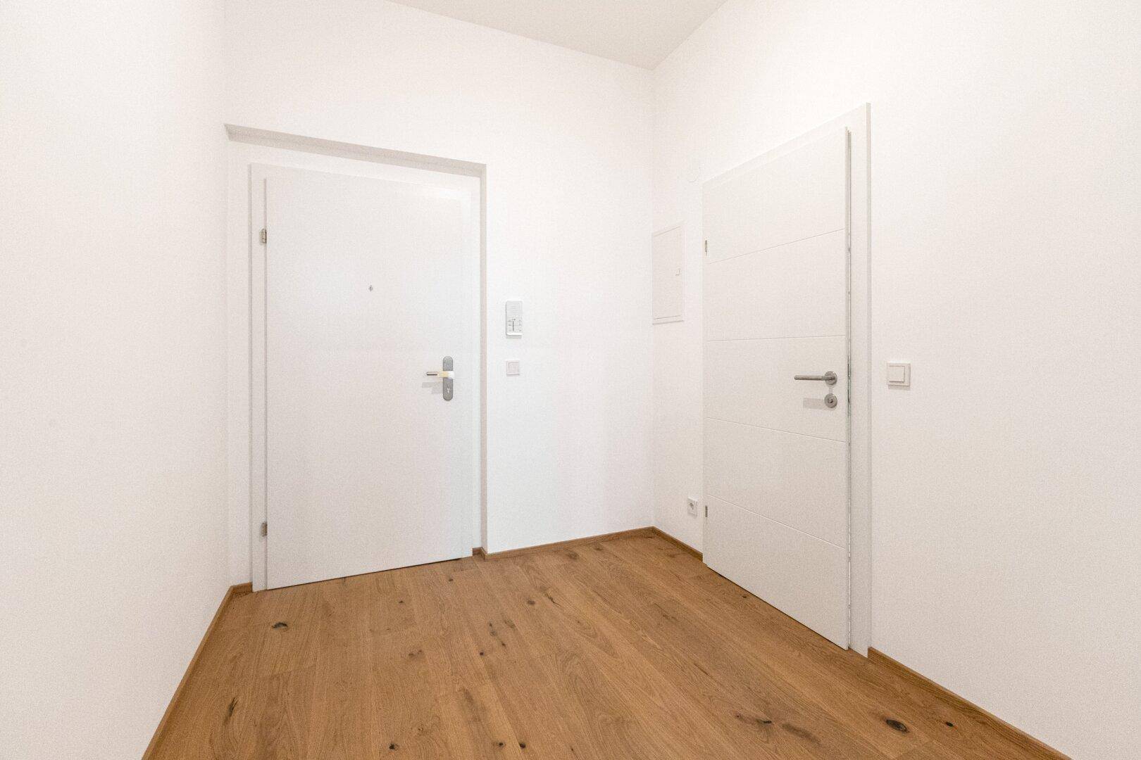 Eingangsbereich mit Holzboden und zwei weißen Türen, die zu den Wohnräumen führen.