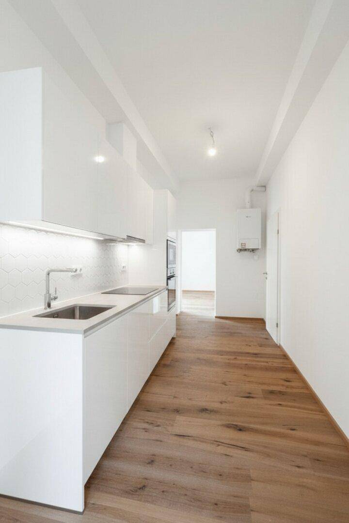 Moderne, schmale Küche mit weißen Hochglanzschränken, integrierten Geräten und Holzboden.