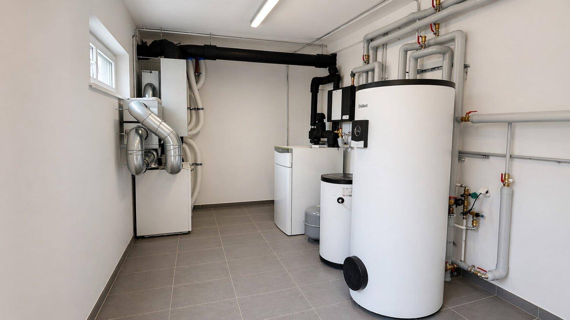 Technikraum mit Heizungsanlage, Warmwasserspeicher und sichtbaren Rohrleitungen.