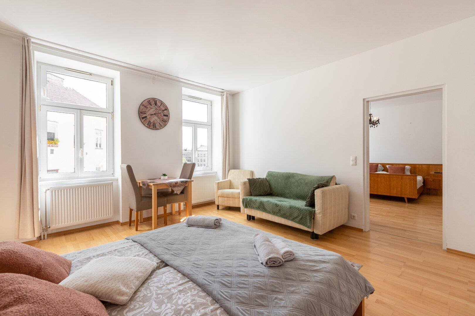 Schlafzimmer mit Holzboden, Doppelbett, Sofa und einem kleinen Esstisch am Fenster.