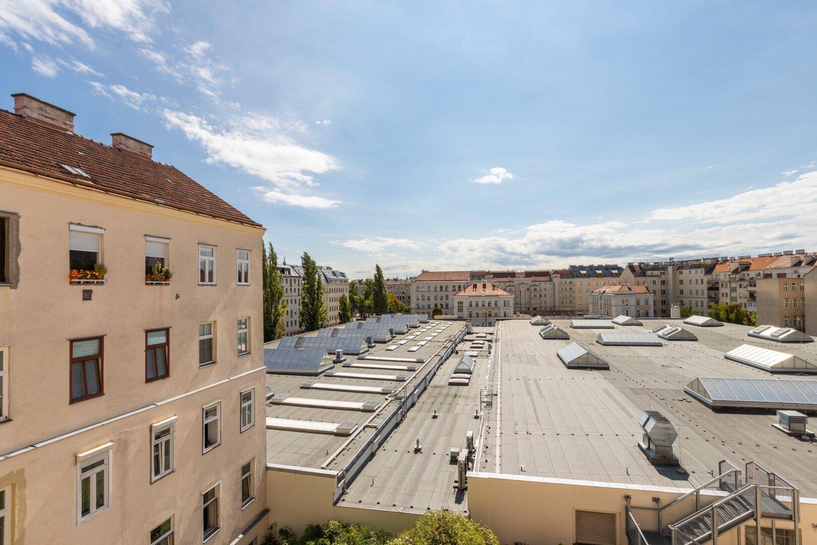 Weitläufiger Blick über die Dächer der Stadt mit angrenzenden Wohngebäuden unter blauem Himmel.