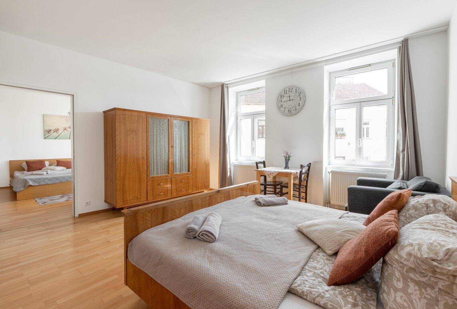 Geräumiges Schlafzimmer mit Holzboden, großem Bett und einem Esstisch am Fenster.