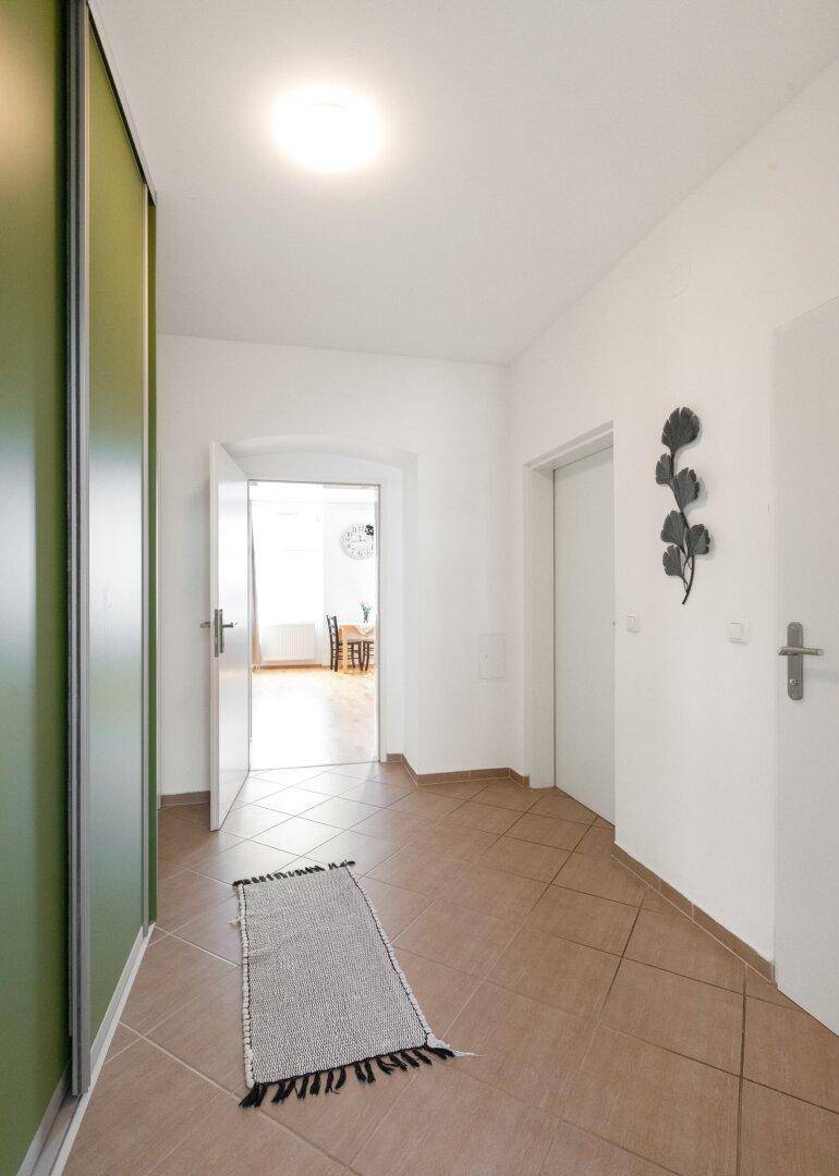 Heller Flur mit Fliesenboden, grünen Schiebetüren und Blick in einen weiteren Raum.