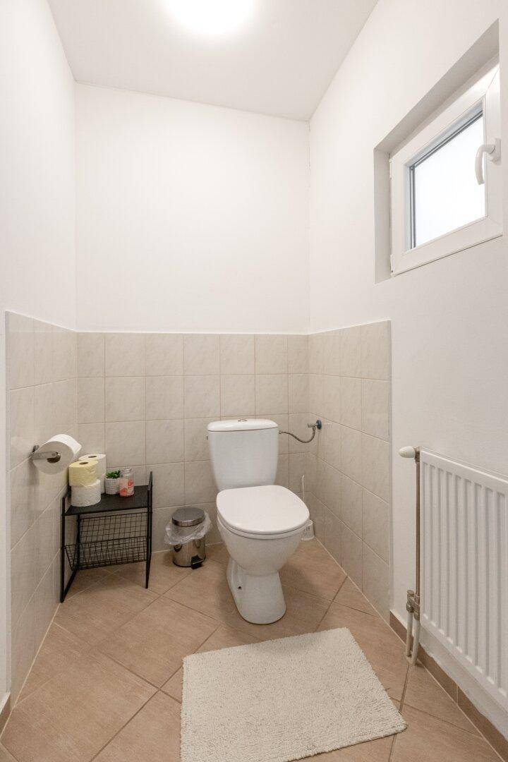 Separate Toilette mit Fenster, Fliesenboden und Heizkörper in einem hellen Raum.