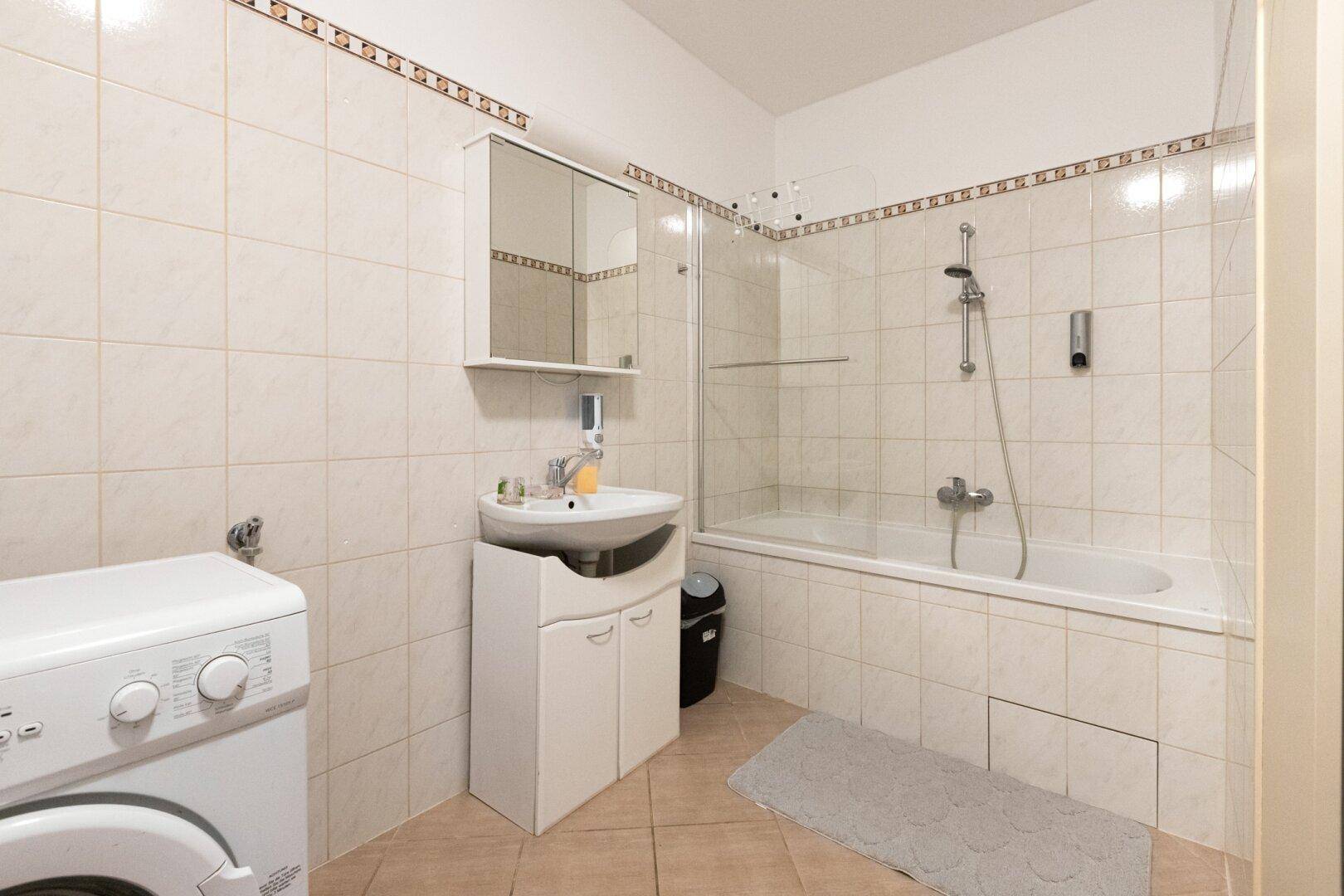 Gefliestes Badezimmer mit Badewanne, Duschabtrennung, Waschbecken und Waschmaschine.