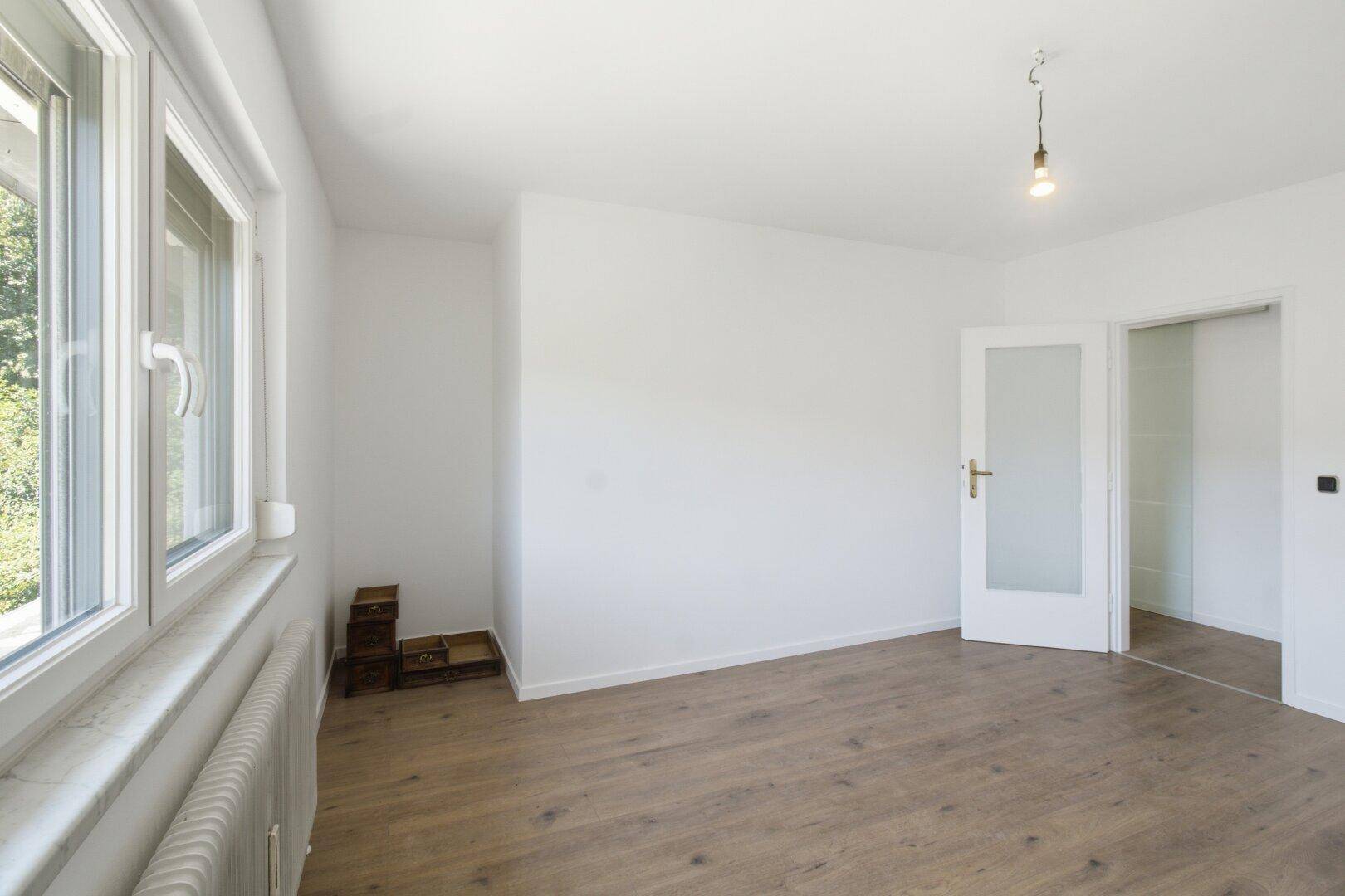 Schlafzimmer mit Laminatboden, großem Fenster und Heizkörper, bietet viel Tageslicht.
