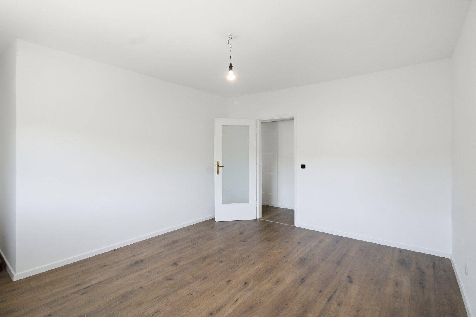 Helles Schlafzimmer mit Laminatboden und weiß gestrichenen Wänden, bereit zur individuellen Gestaltung.