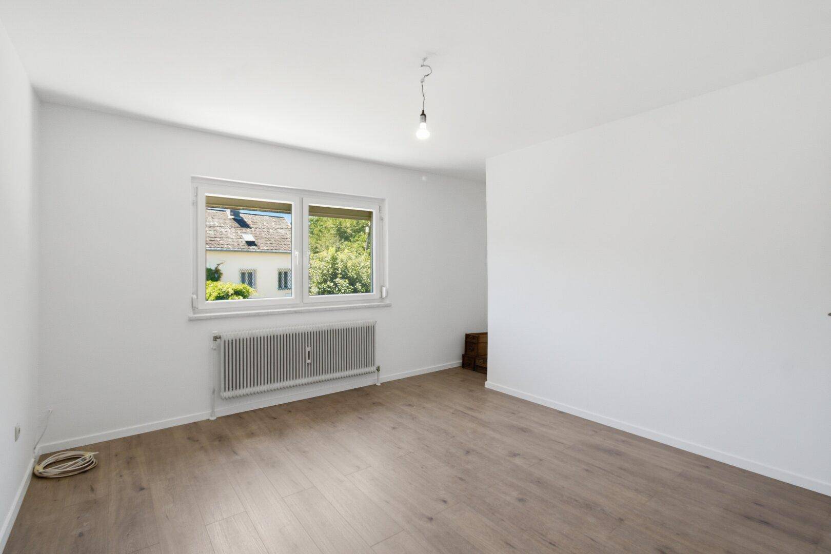 Unmöbliertes Schlafzimmer mit Laminatboden, großem Fenster und Blick auf die Nachbarschaft.