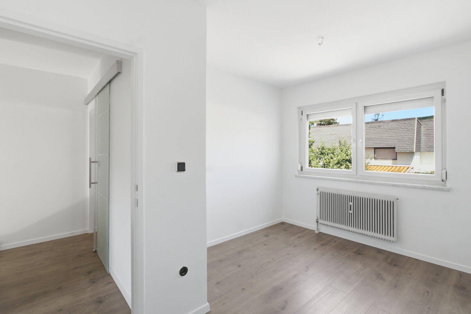 Geräumiges Schlafzimmer mit Laminatboden, Schiebetür und großem Fenster mit Ausblick.