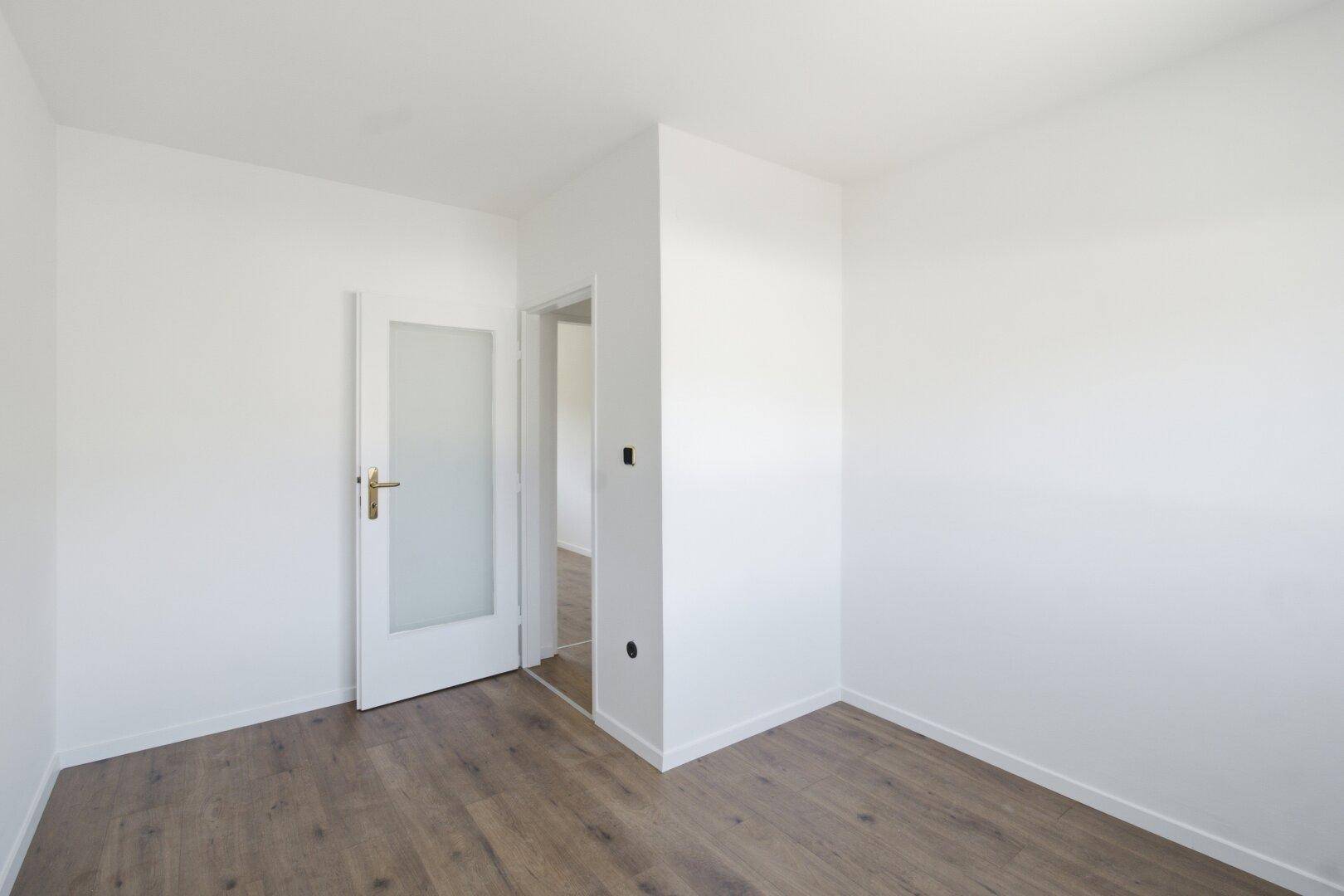 Leeres Schlafzimmer mit Laminatboden und weiß gestrichenen Wänden, bereit zur Einrichtung.