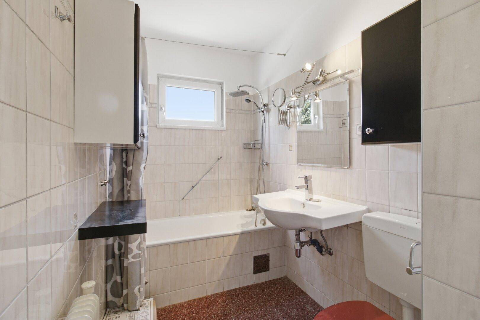 Gefliestes Badezimmer mit Badewanne, Waschbecken und Fenster, in hellem Design.