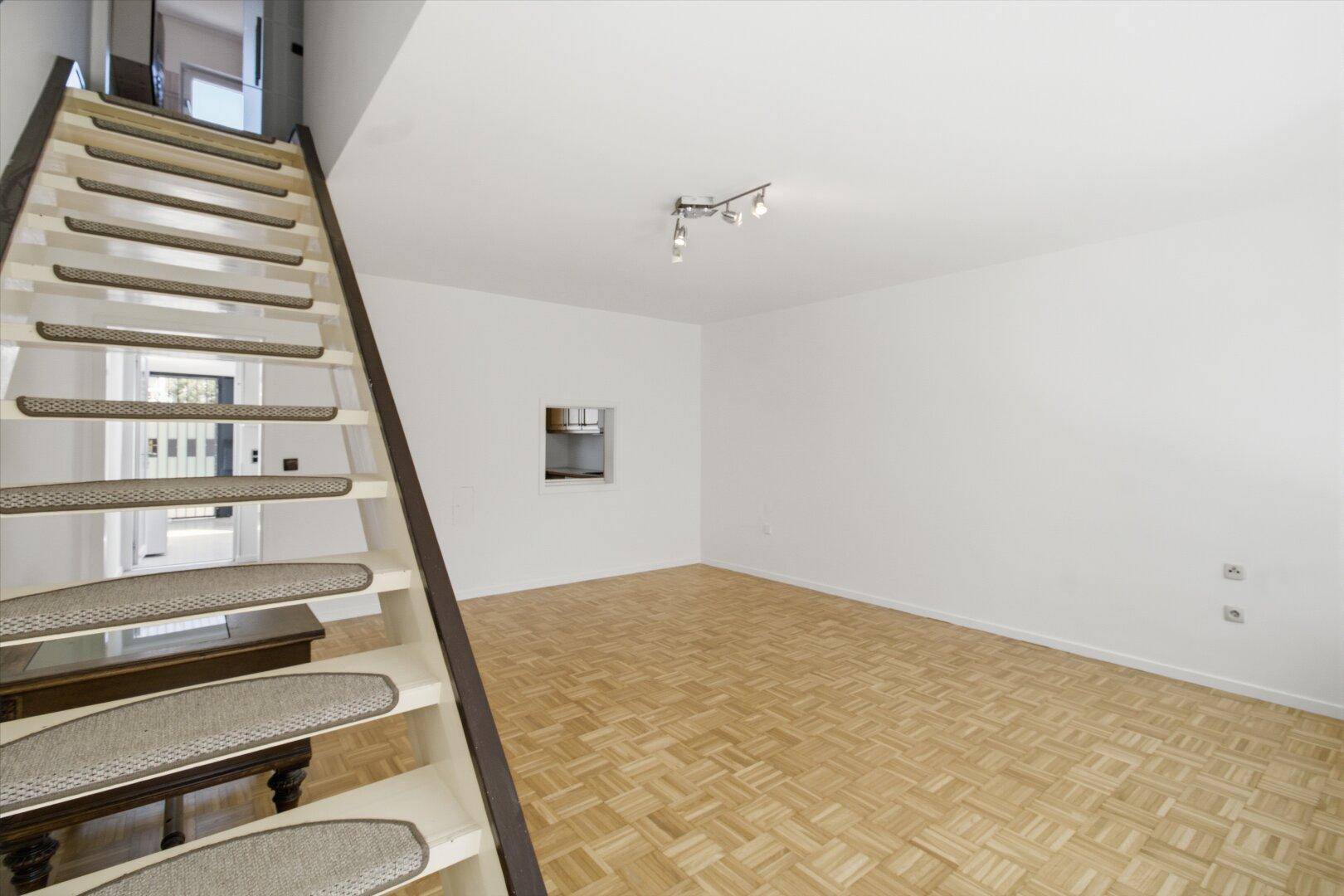 Blick auf die offene Treppe im Wohnbereich mit Parkettboden und weiß gestrichenen Wänden.