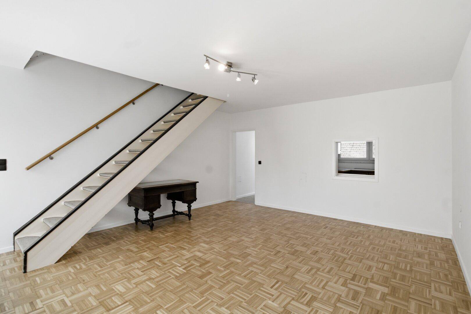 Heller Wohnbereich mit Parkettboden und offener Treppe, die in das obere Stockwerk führt.