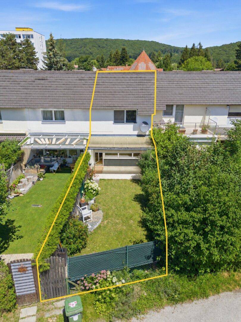 Luftaufnahme eines Reihenhauses mit Garten und Grundstücksgrenzen, umgeben von Bäumen.