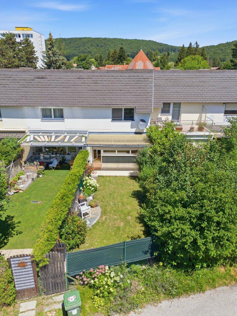 Luftaufnahme eines Reihenhauses mit gepflegtem Garten und überdachter Terrasse im Grünen.
