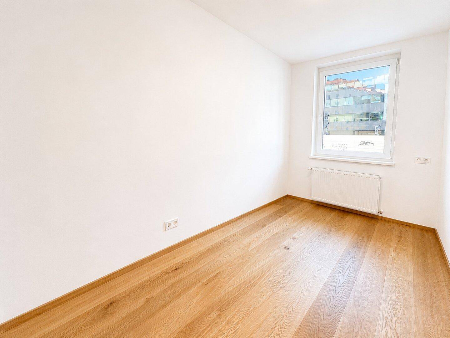 Unmöbliertes Zimmer mit hellem Holzfußboden und großem Fenster.