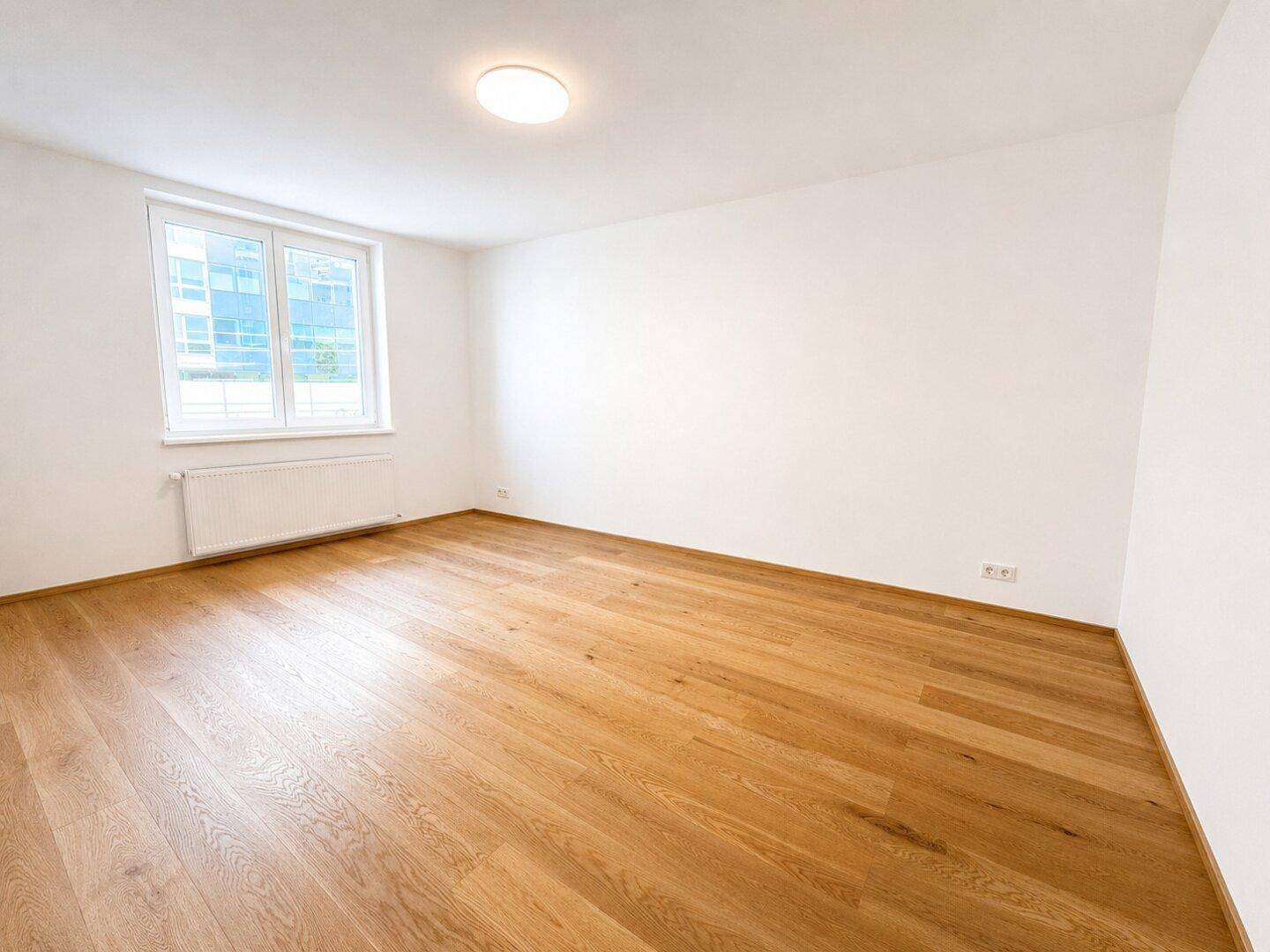 Geräumiges, unmöbliertes Schlafzimmer mit hellem Holzfußboden und großem Fenster.