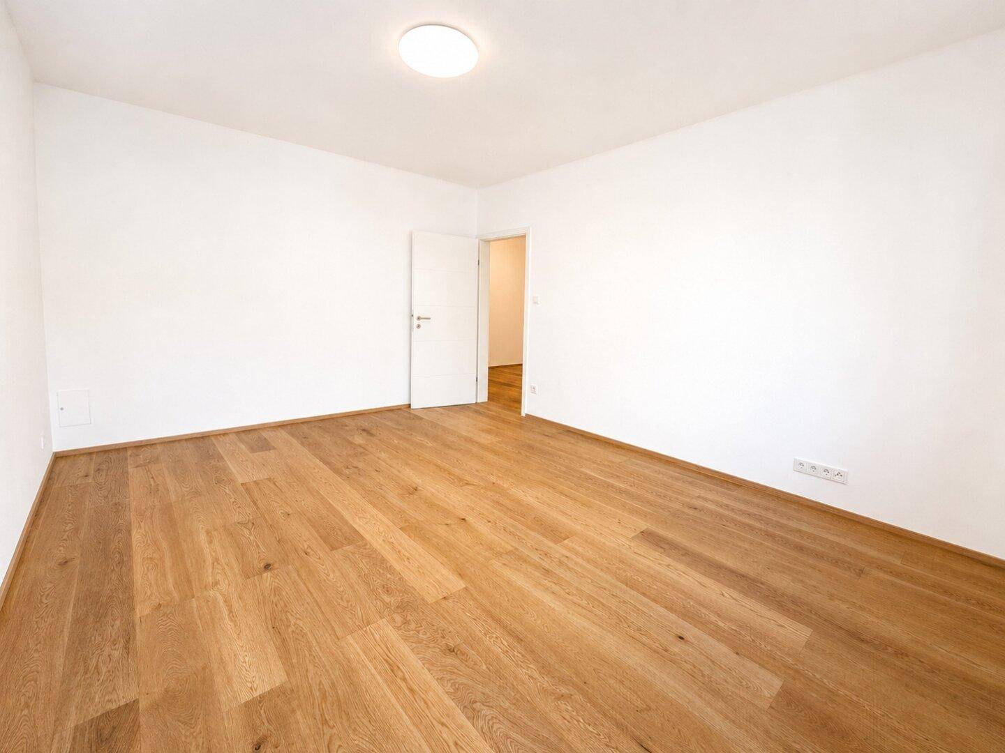 Heller Schlafbereich mit Holzparkett und Zugang zu weiteren Räumen.