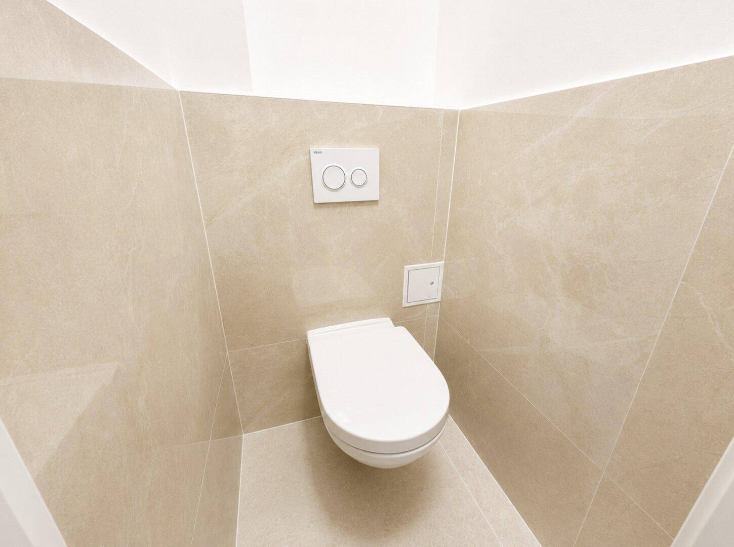 Separates WC mit wandhängender Toilette und modernen Fliesen.