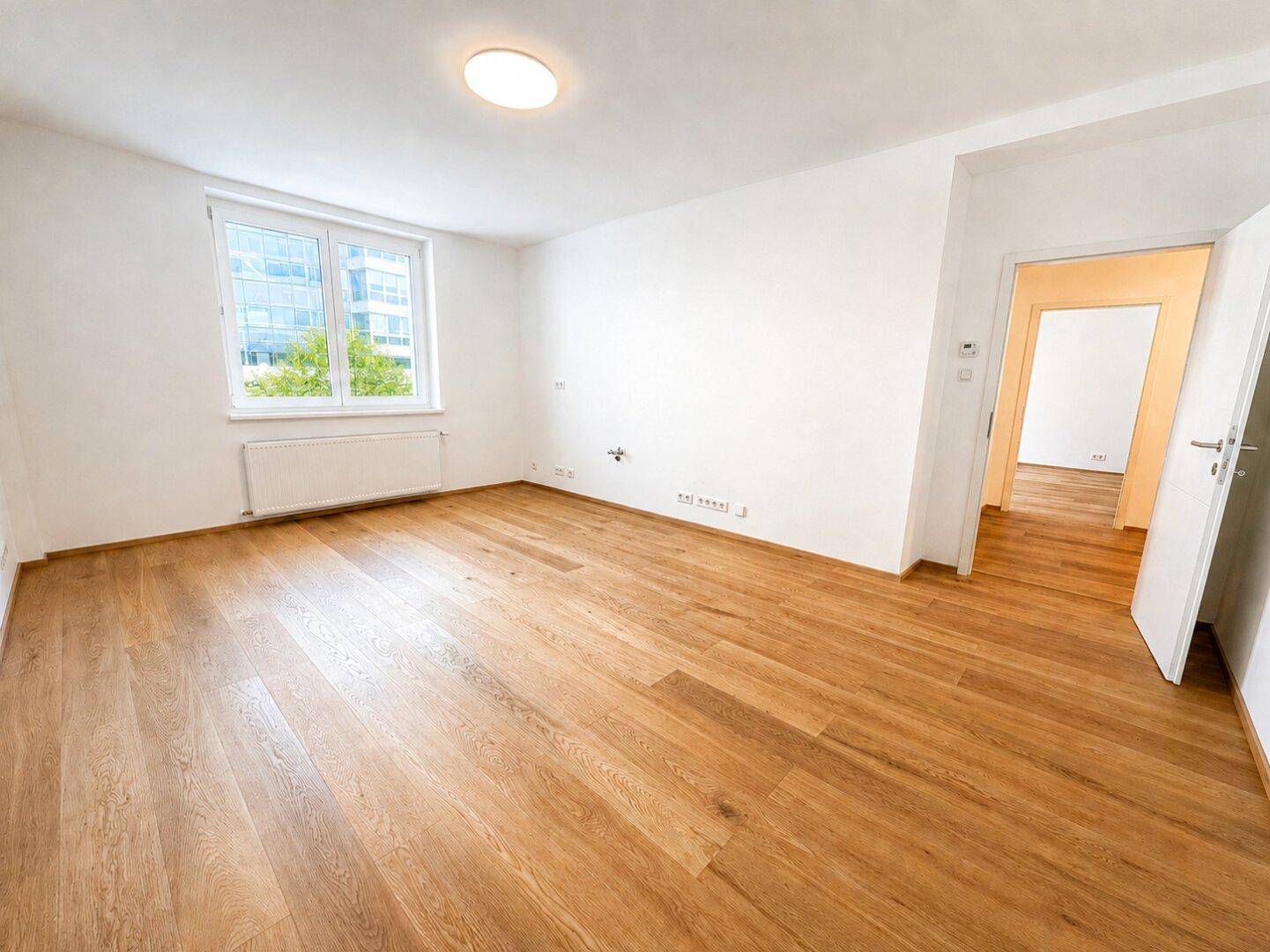 Heller, leerer Raum mit neuem Holzfußboden und Blick auf moderne Gebäude.