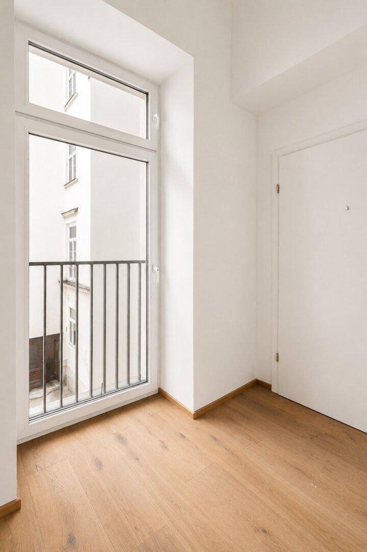 Heller Raum mit französischem Balkon und Holzboden.