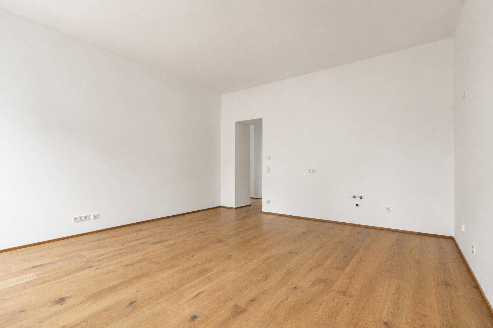 Geräumiger, leerer Wohnraum mit hellem Parkettboden und weißen Wänden.